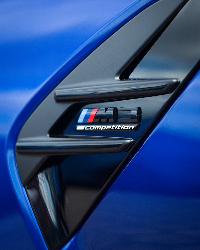 Detailed view of the sleek BMW M3 Competition badge on a vibrant blue car.